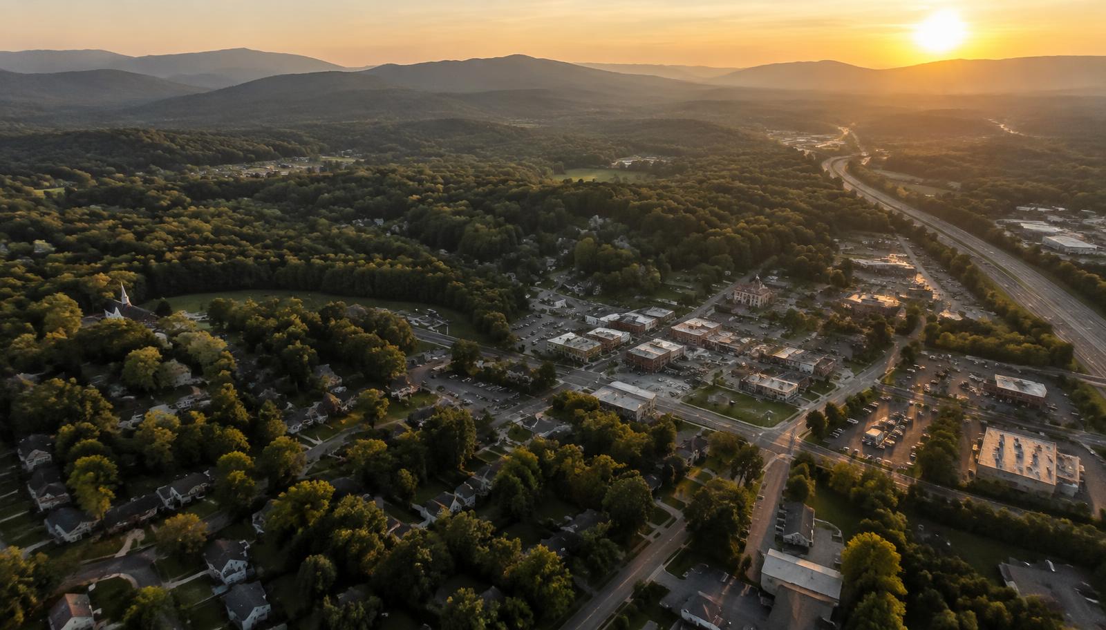 Aerial view of a wooded North Georgia county at golden hour with neighborhoods and a highway corridor